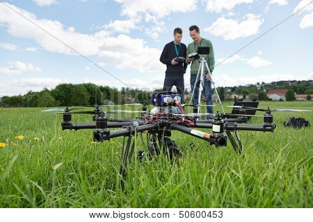 UAV octocopter on grass with engineers discussing in background at park