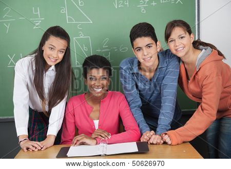 Portrait of young teacher with high school students at desk in classroom