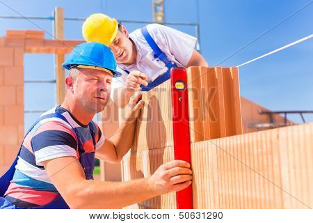 Construction site workers or bricklayer with helmets controlling building walls with a bubble level 