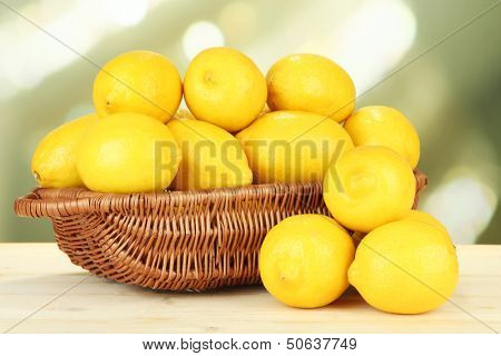 Ripe lemons in wicker basket on table on bright background