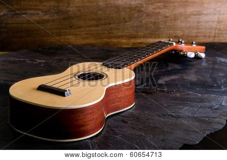 old ukulele against a black stone background.