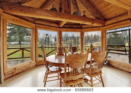 Bright dining room in log cabin house with floor-to-ceiling windows rustic dining table set and cathedral ceiling with beams.