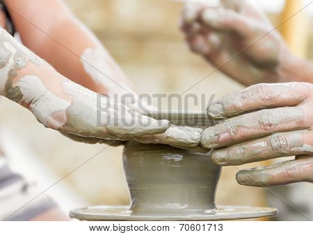 child learning how to make a pot on a pottery wheel, old potter helps