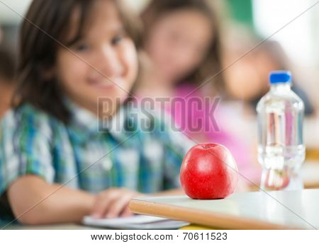 Happy little boy with apple and water bottle sitting in classrom and smiling