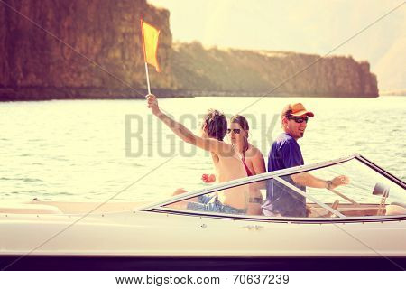 a bunch of people on a boat with one waving a flag indicating a water skier in the water toned with a retro vintage instagram filter effect