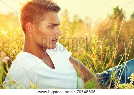 Handsome guy lying on the field. Young man enjoying nature outdoors.  