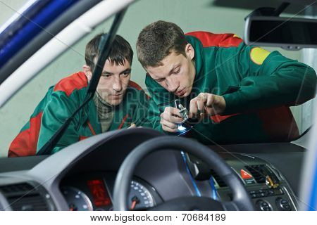Automobile glazier repairman teaching or discussing with partner windscreen repair of a car in auto service station garage