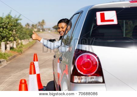 beautiful african learner driver looking out of the car window and giving thumb up