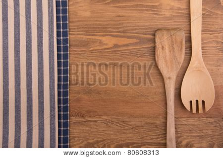 Wooden kitchen utensils and linen kitchen towels on dark wood tabletop, with copy space in the center