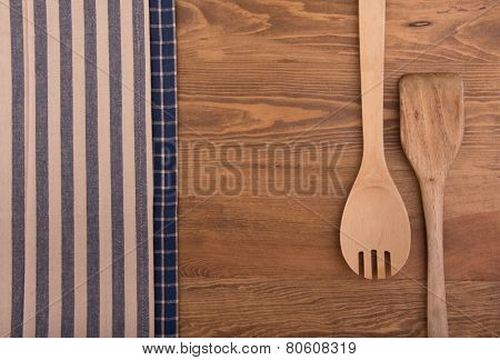 Wooden kitchen utensils and linen kitchen towels on dark wood tabletop, with copy space in the center