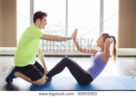 fitness, sport, training, teamwork and people concept - happy woman with personal trainer doing sit ups and high five gesture in gym