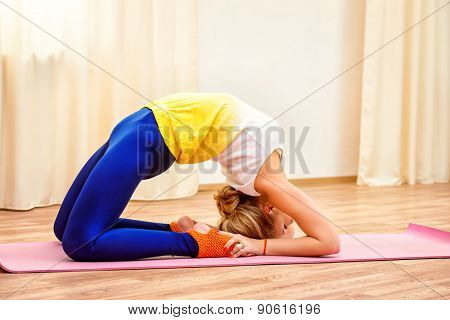Slender athletic girl doing yoga exercises indoor. Backbend.