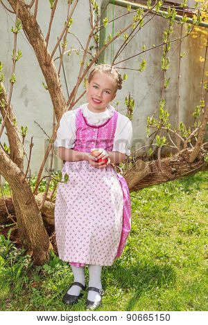 Girls in the dirndl sit in the garden and plays laughing with Easter eggs