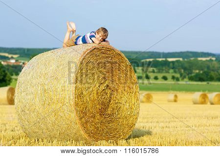 Little kid boy sitting on hay bale in summer