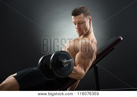 Determined Man Exercising With Dumbbells On Chair