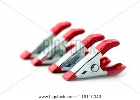 Spring Clamps Of Metal With Red Handles In A Row Isolated On A White