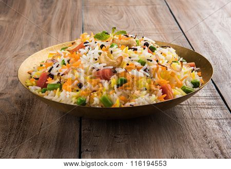 Veg biryani or veg pulav served in a round brass bowl over wooden background