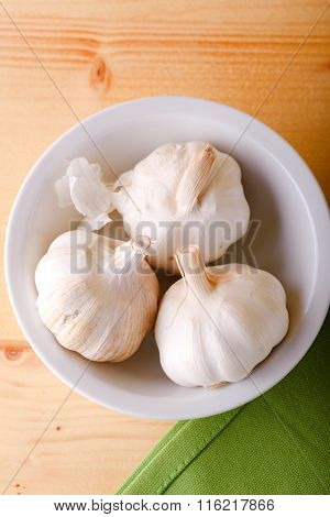 Three Garlic Bulbs In White Ceramic Bowl