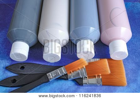 Four bottles with acrylic paint and brushes, on blue background for handmade, hobby and decoration