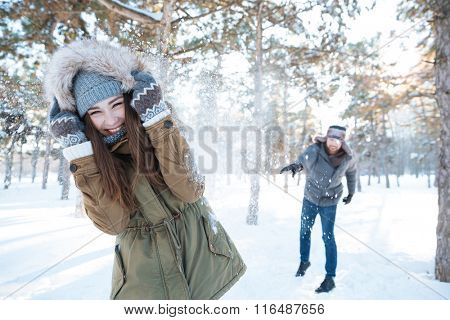Beautiful happy couple throwing snowballs and having fun in winter park