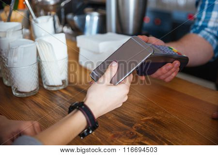 Woman paying for coffee by mobile phone and using reader holded by waiter in cafe