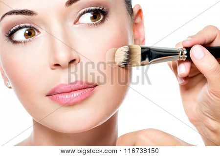 Makeup artist applying liquid tonal foundation  on the face of the woman