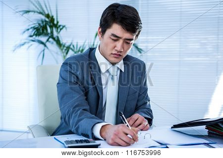 Riled up asian businessman in his desk and writing somethings