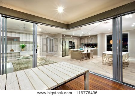Inside View Of A Modern House Lights Turned On With Wooden Table  Sorrounded By Glass Doors.