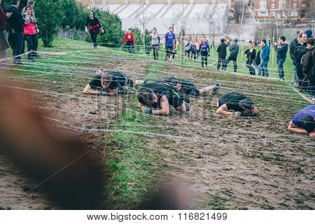 Runners crawling under barbed wire in a test of extreme obstacle race