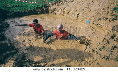 Runners crossing mud pit in a test of extreme obstacle race