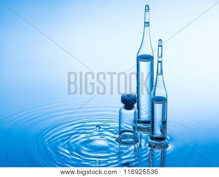 Medical ampoules and bottle  on the blue water background with splash and drops