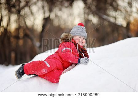 Little boy in red winter clothes having fun with fresh snow. Active outdoors leisure with children in winter. Kid during stroll in a snowy winter park