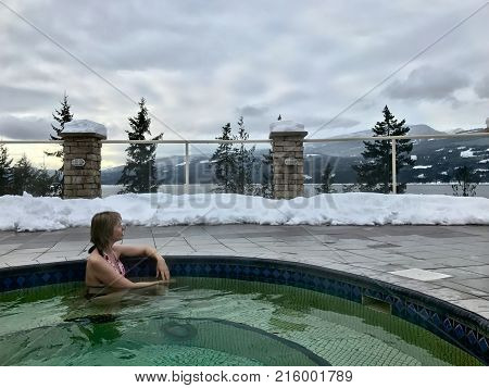 Woman in Hot Springs Pool with hot mineral healing water. Winter season in Canadian Rockies. Hot mineral pool surrounded with mountains trees and snow. British Columbia. Canada.