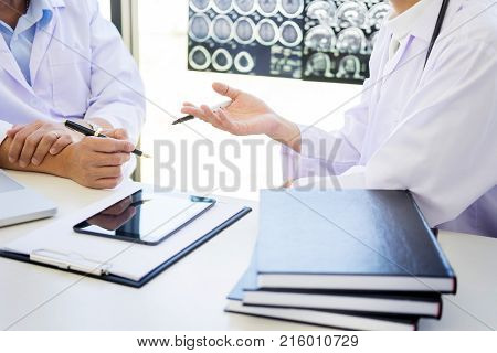 Two doctors analyzing a scan or x-ray film or explains a CT scan together with serious thoughtful expressions method with patient treatment results on brain to an anomaly on the film