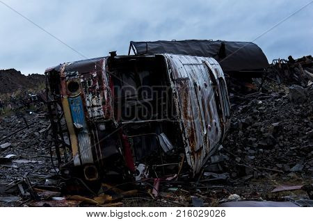 old abandoned bus in the middle of a rusty trash can against a dark evening sky