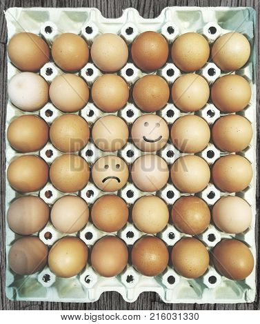 brown eggs in carton with happy and sad face painted onto two of them