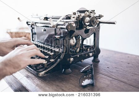 close-up of man using vintage manual typewriter on rustic wooden table