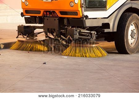 Yellow urban sweeper cleans road from dirt with a round brush