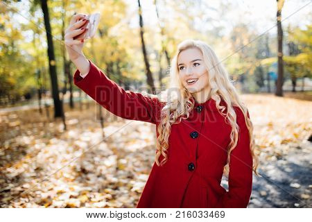 Teenage Girl In Autumn In Park Taking A Selfie On Smart Phone. Beautiful Happy Young Woman Taking A