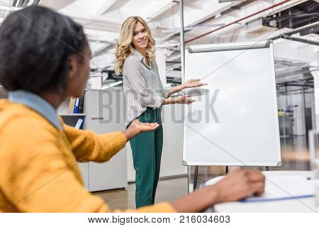 young manageress makig presentation with blank whiteboard for her colleague
