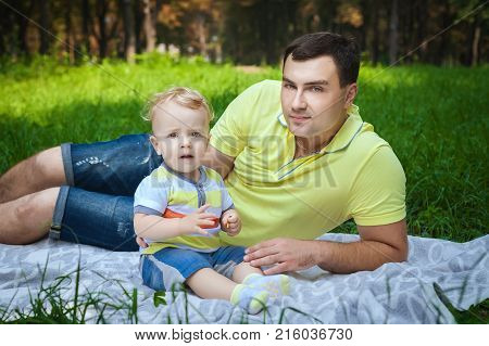 handsome guy resting with his son in forest, healthy young man playing with little son in city park