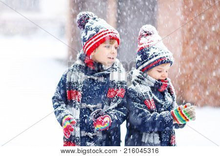 Two little kid boys in colorful fashion clothes playing outdoors during strong snowfall. Active leisure with children in winter on cold days. Happy siblings and friends having fun with first snow