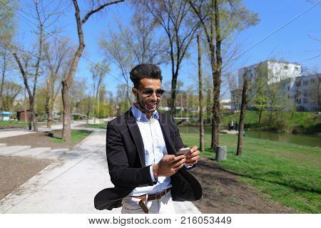 Man hold phone in hand and talking with mom. Son has dimple on cheeks, beard, short hair and long nose. Person dressed in black jacket and blue shirt. Concept of new apps modern technologies and long talks and cheep tariff plans.