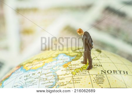 Miniature figure country leader man standing and looking at north korea map on globe as world critical nuclear missile war situation or war talk negotiation concept.