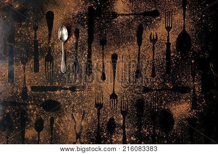 Vintage tablespoon and shapes of disappeared cutlery under brown dust over black metal background. Top view