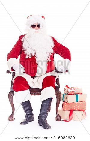 Portrait of swaggy Santa Claus in sunglasses relaxing in chair on white background