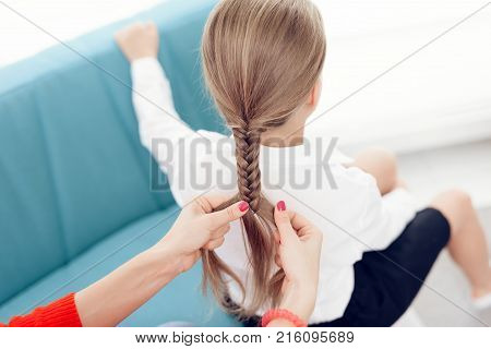 Mother collects her daughter to school. The mother braids her daughter's hair. A woman plaits a braid a little girl.