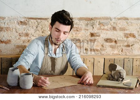 Handsome Young Mexican Potter Does Sketches Of Ceramics On The Paper. Concept Of Small Business, Han
