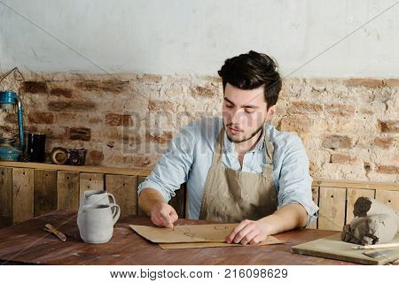 Handsome Young Mexican Potter Does Sketches Of Ceramics On The Paper. Concept Of Small Business, Han