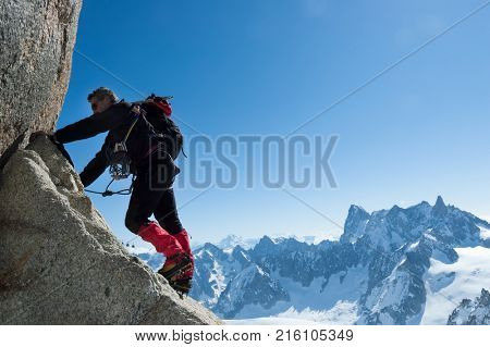 Climbing in Chamonix. Climber on the stone wall of Aiguille du Midi in Mont Blanc, France. Large copy-space on the right. Concepts: determination, concentration, effort, strength, team work.